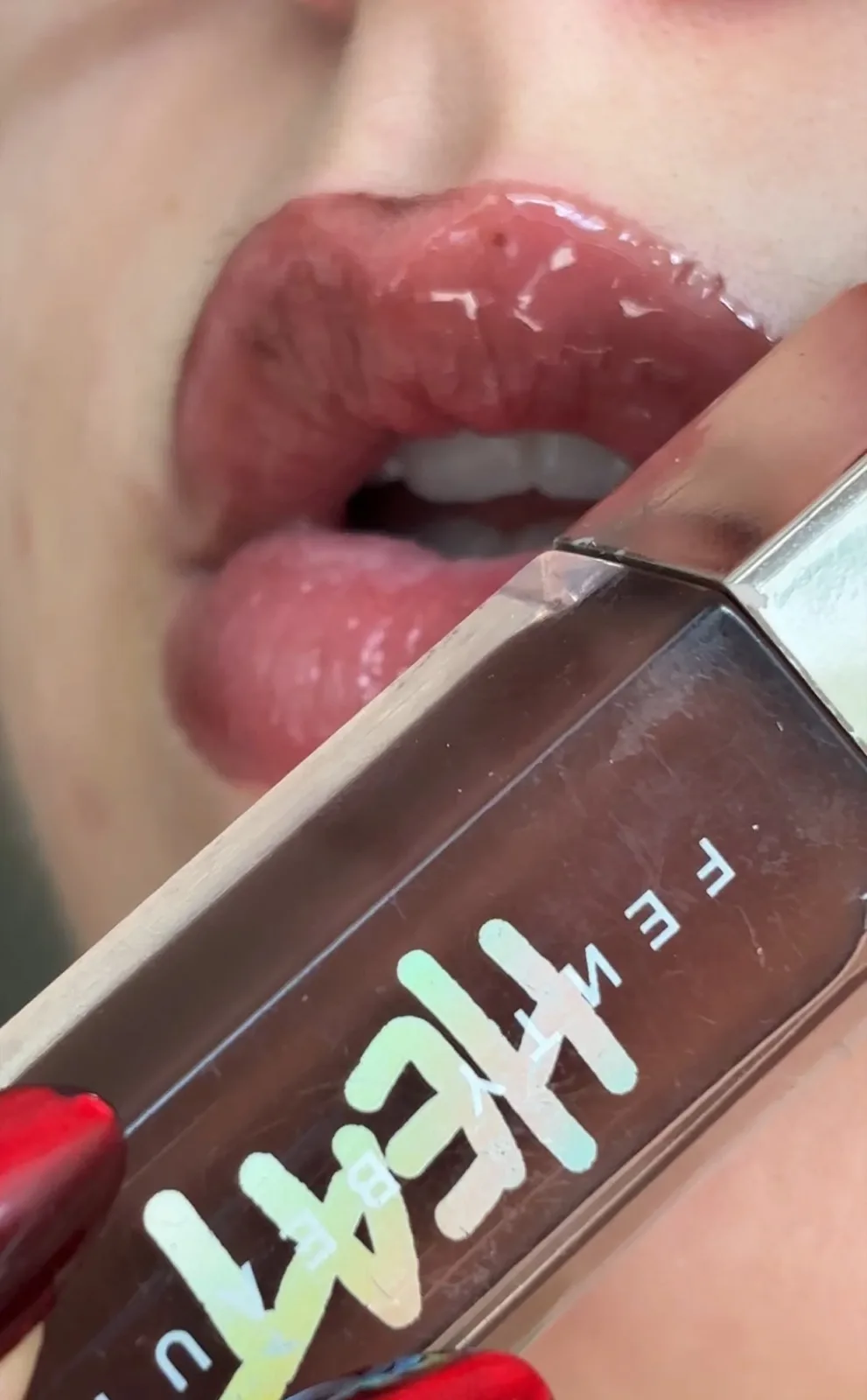 Close-up of glossy lips holding Fenty Beauty lip gloss
