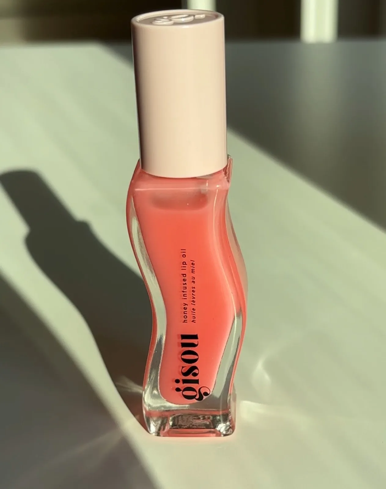 Gisou honey infused lip oil photographed in sunlight with soft shadows