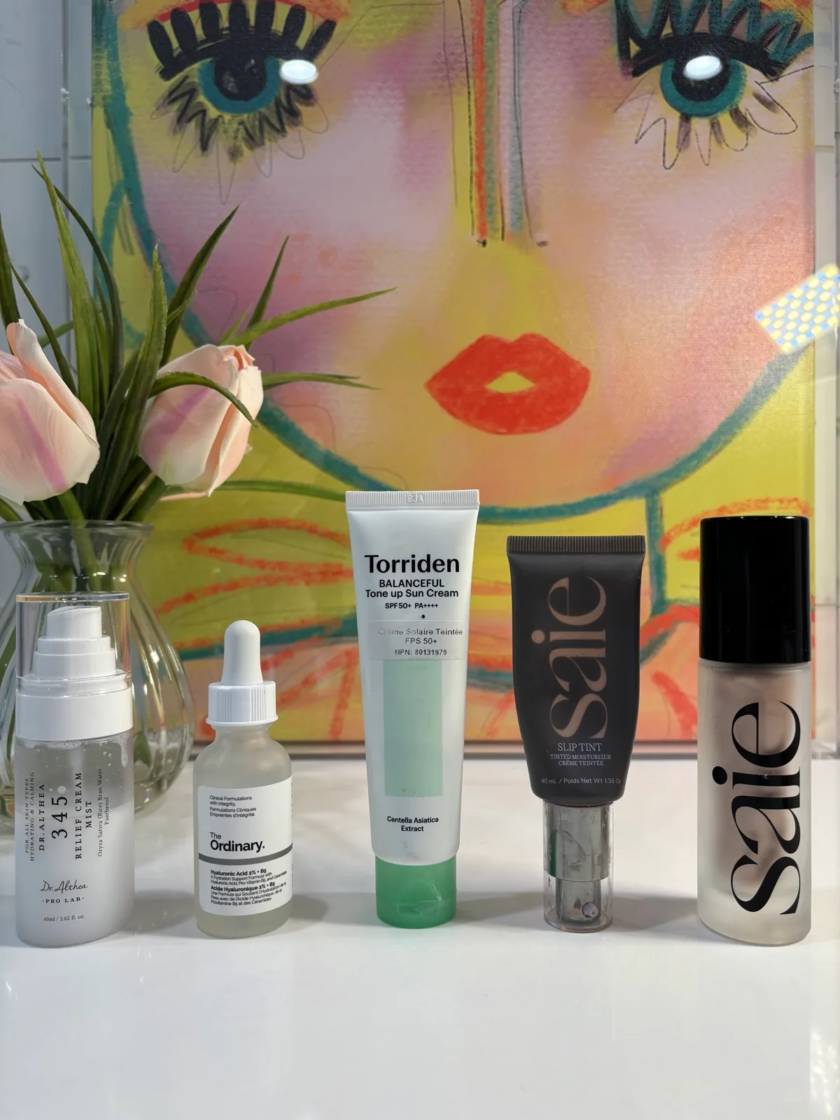 Morning skincare products lined up beside flowers and colorful artwork